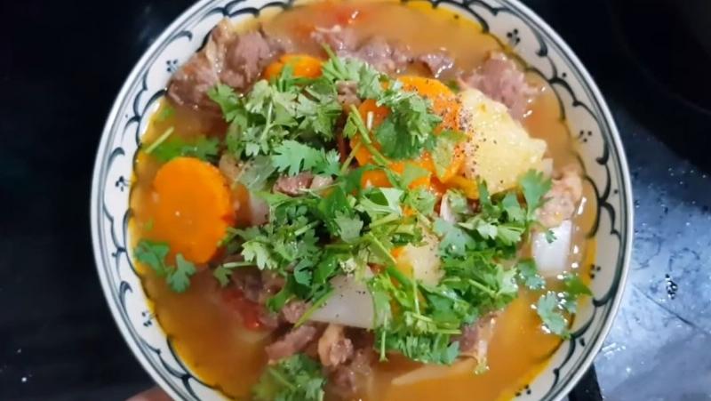 Hình ảnh nồi thịt bò hầm khoai tây đang sôi nhẹ trên bếp, các miếng thịt bò, khoai tây và cà rốt ngập trong nước sốt sền sệt đậm màu