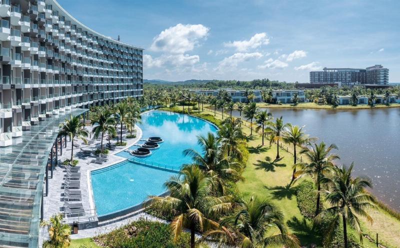 Một resort sang trọng với hồ bơi vô cực nhìn ra bãi biển Hồ Cốc, bao quanh là cây xanh.